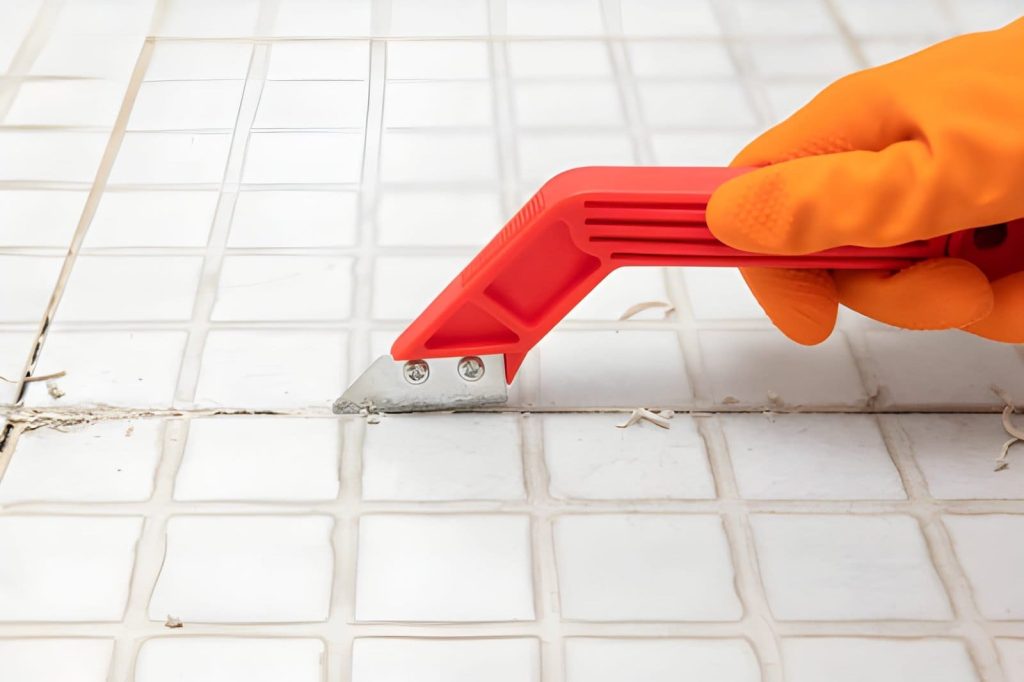 Tile regrouting Melbourne—hand in orange glove using grout removal tool on ceramic tiles.